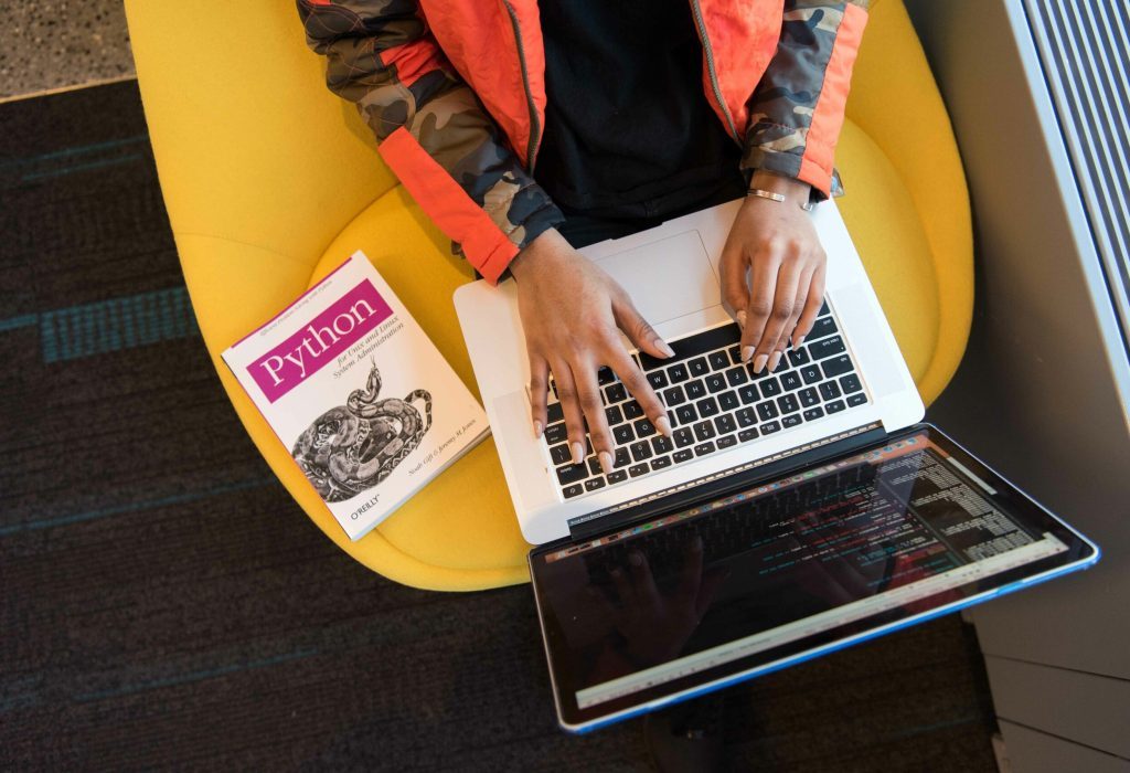 stock image of a woman typing on computer with python coding book