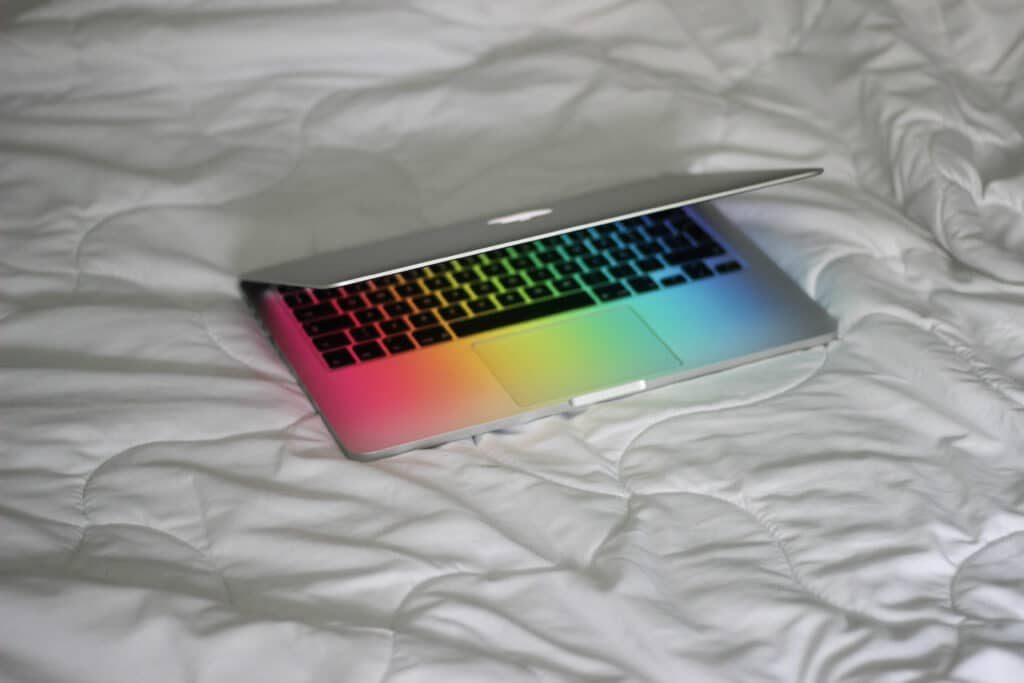 Laptop on a desk lit with rainbow-colored light